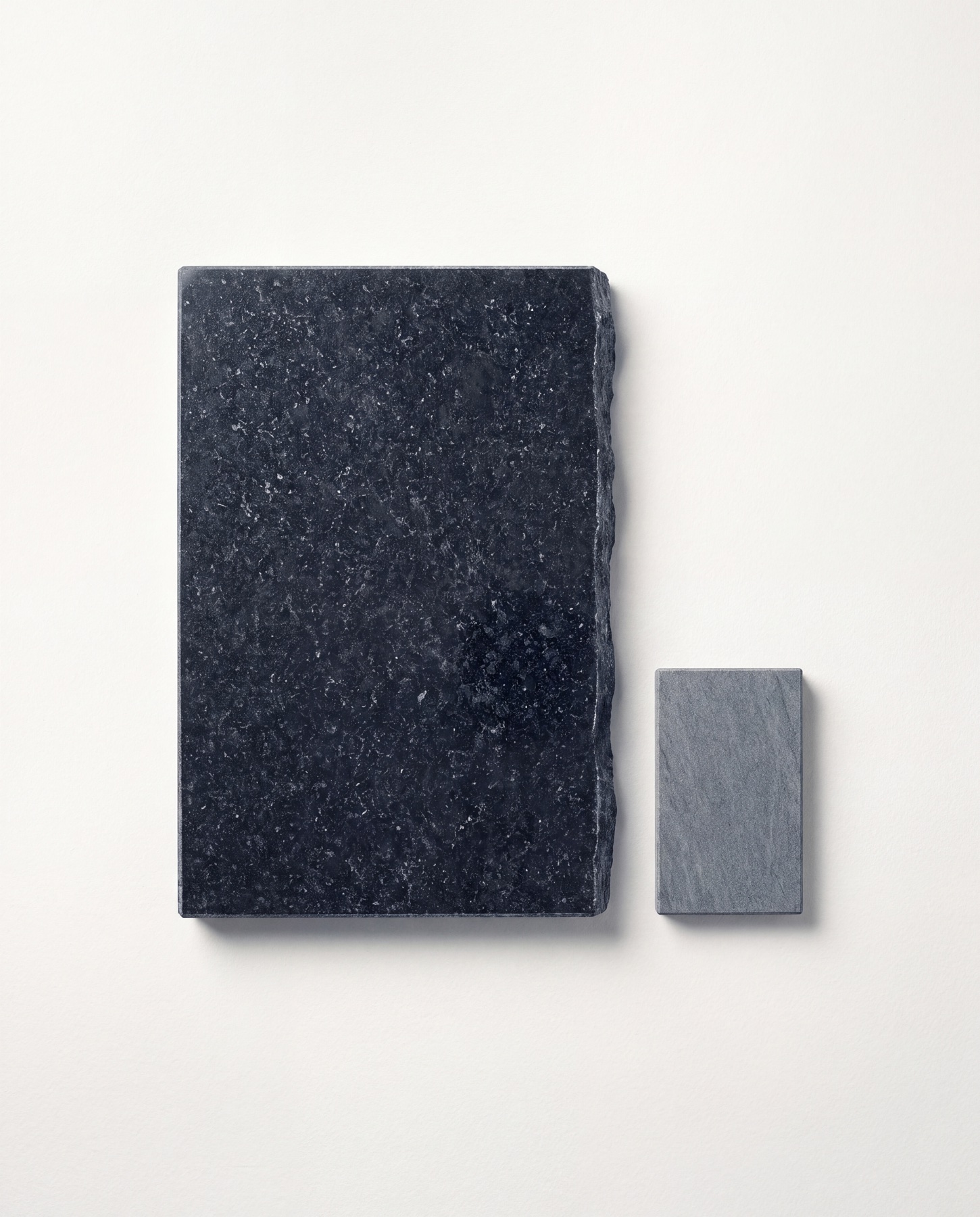 A Black Pearl granite jumbo slab and a Fine Grey sample on a paper-white studio ground.